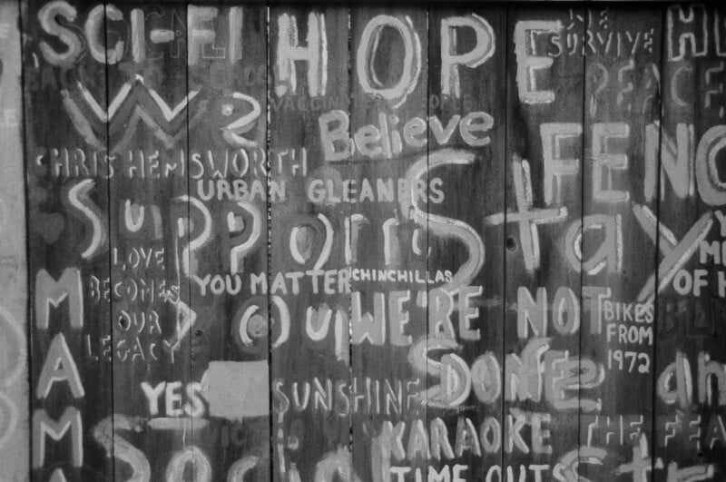 A wooden wall covered in white graffiti with words and phrases like “HOPE,” “Believe,” “YOU MATTER,” “STAY,” “LOVE BECOMES OUR LEGACY,” and other partially visible positive messages.
