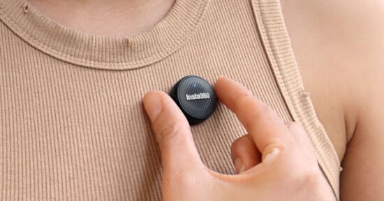 A person wearing a beige ribbed tank top attaches a small round Insta360 camera to their chest, holding it in place with their fingers.