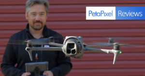 A man stands in front of a red wall, holding a controller, while a camera drone hovers in the foreground. The image features a "PetaPixel Reviews" logo in the top right corner.