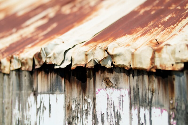 Close-up of a weathered, rusty corrugated metal roof and wall with peeling paint and visible rust streaks, suggesting age and exposure to the elements.