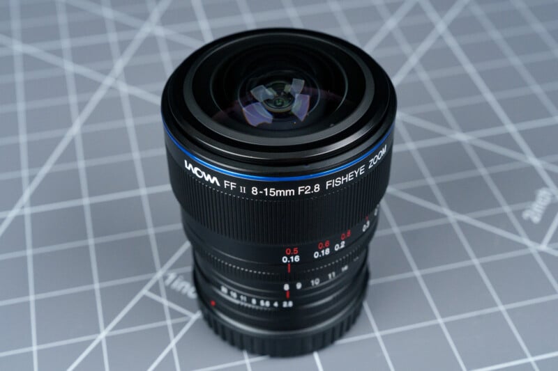 A Laowa FF II 8-15mm F2.8 fisheye camera lens stands upright on a gray cutting mat with a grid pattern.