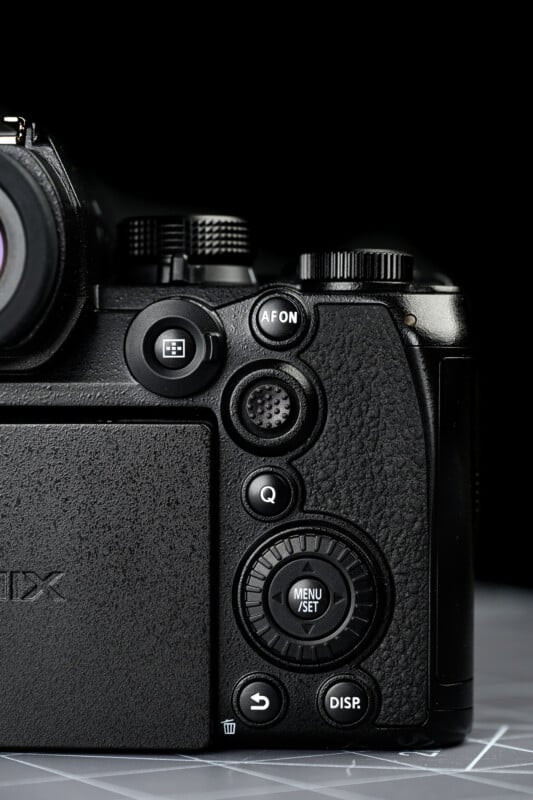 Close-up of the back right side of a black digital camera, showing several control buttons, dials, and part of the LCD screen, all against a dark background.