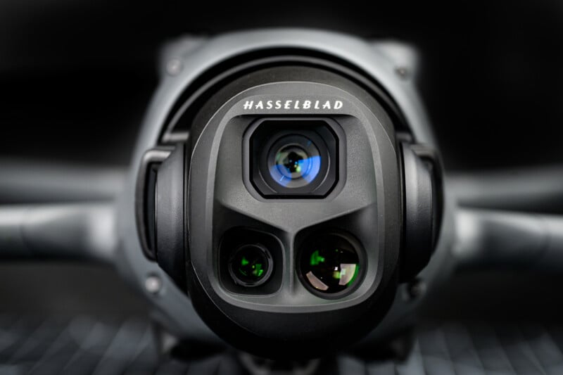 Close-up view of a Hasselblad camera lens mounted on a drone, with multiple circular lenses and a black, sleek exterior, set against a dark, blurred background.
