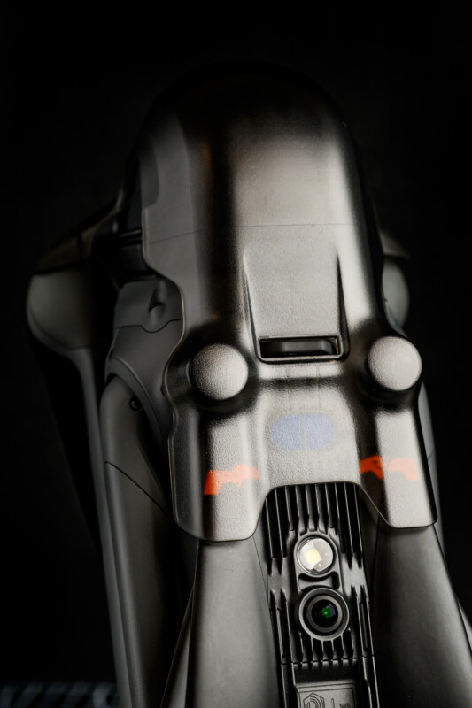A close-up of a sleek, black robotic device with a smooth, curved design, circular features, and a camera lens near the base, set against a dark background.