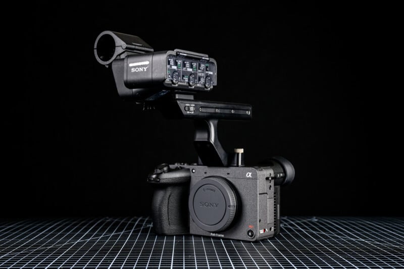 A Sony Alpha cinema camera with an audio interface and microphone mount attached, positioned on a grid-patterned surface against a black background.