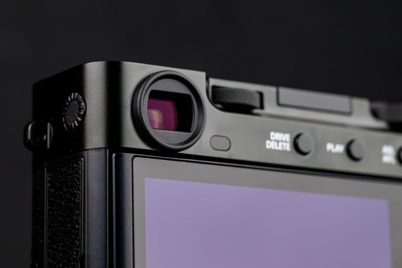 Close-up of the top rear corner of a digital camera, showing the viewfinder, several buttons, and part of the LCD screen. The background is dark and out of focus.