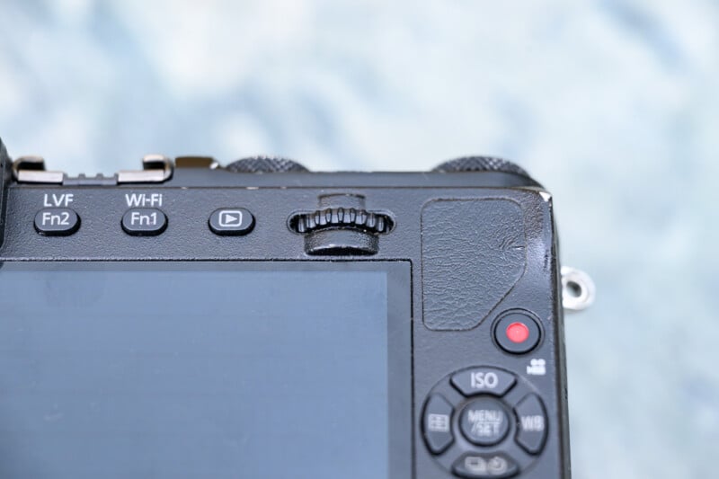 Close-up of the back of a digital camera showing part of the screen and various buttons, including ISO, menu, and red record button, as well as Wi-Fi and function buttons.
