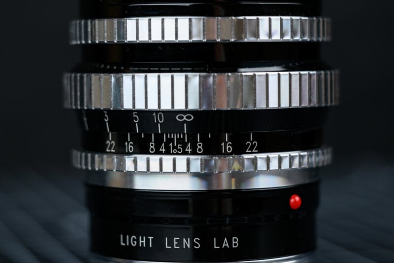 Close-up of a camera lens focusing ring showing distance and aperture markings, with the brand "LIGHT LENS LAB" and a red indicator dot visible on the lens barrel.