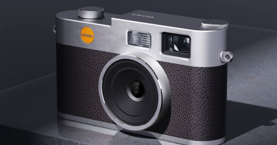 A modern digital camera with a metallic silver body, textured black grip, and a large lens, placed on a gray stone surface under soft lighting.