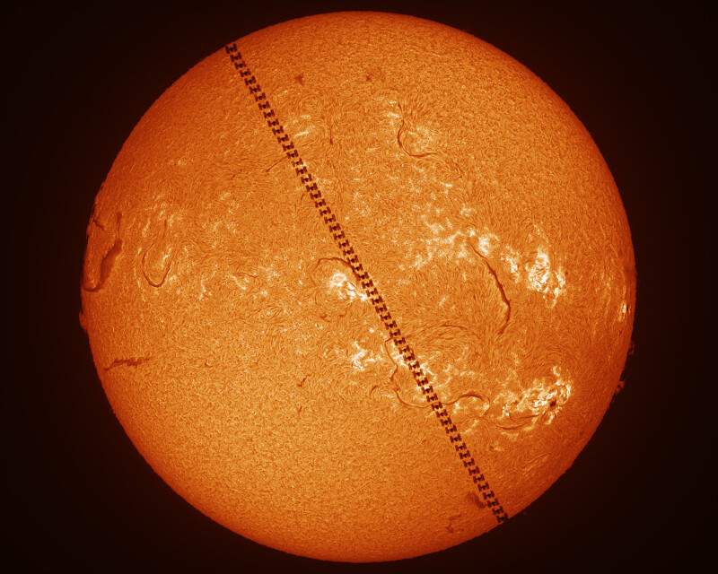 An orange, detailed image of the Sun with a dotted, diagonal black line crossing it, representing the silhouette of the International Space Station transiting in front of the Sun.
