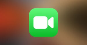 A green square icon with rounded corners featuring a white video camera symbol in the center, commonly used to represent video calling or conference applications. The background is blurred with warm tones.