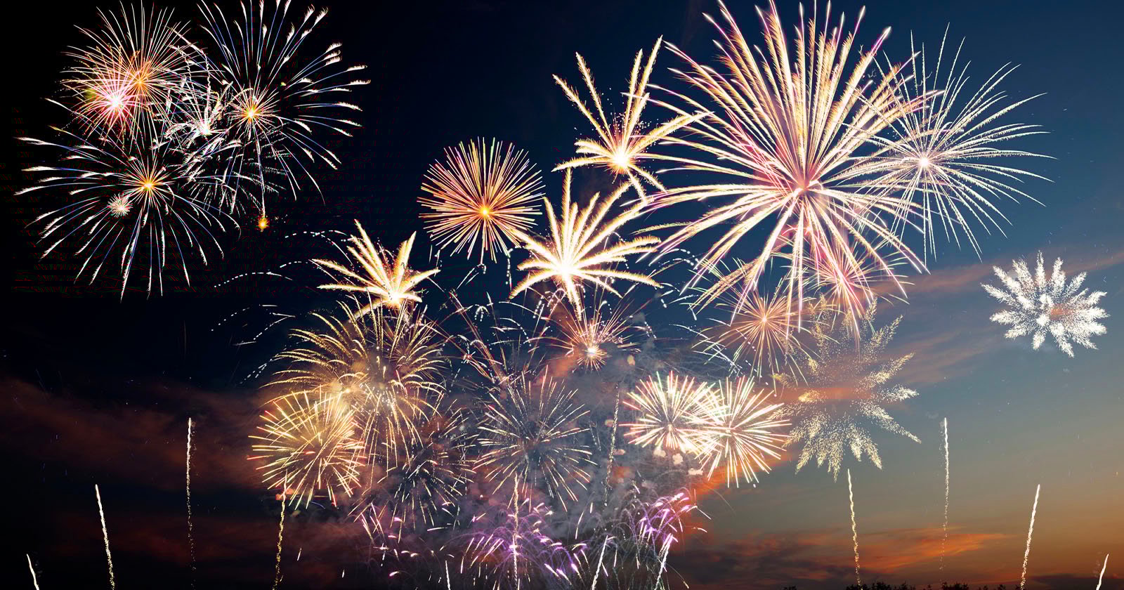 Bright, colorful fireworks burst and sparkle in the night sky over a dark landscape, creating a festive and celebratory atmosphere.