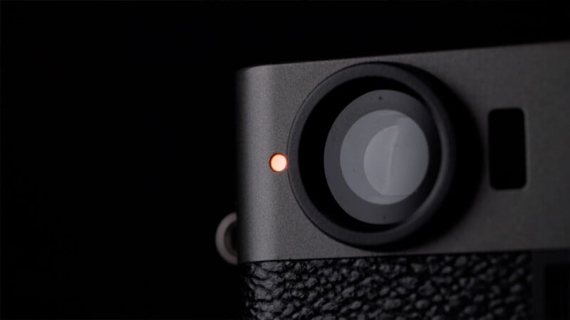 Close-up of a camera lens in the top right corner, with a small orange indicator light next to it, set against a dark background.