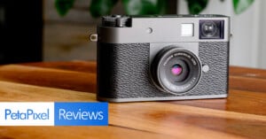 A classic-style digital camera with a textured black body rests on a wooden surface. The lens reads “SUMMICRON ASPHERIC.” In the lower left, the PetaPixel Reviews logo is displayed.