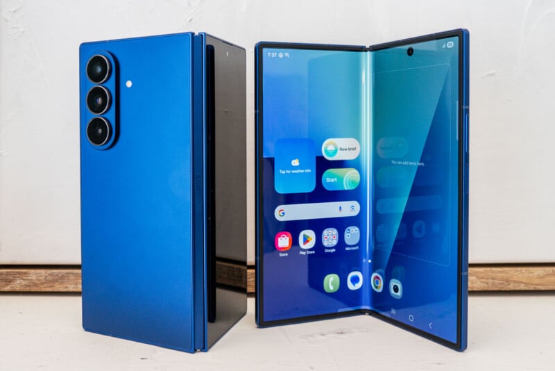 A blue foldable smartphone is shown, with one device folded shut displaying the back with three cameras, and another opened to reveal its large inner touchscreen and various app icons.