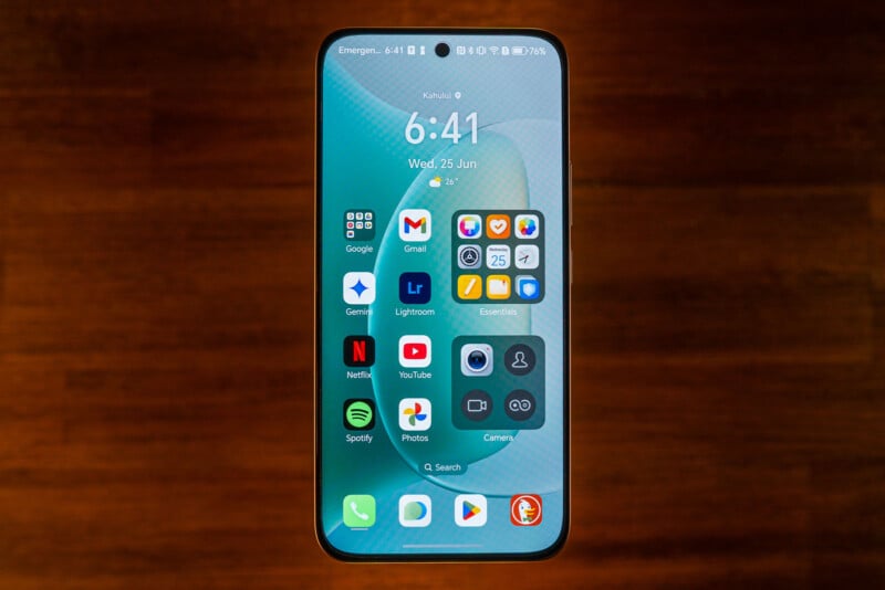 A smartphone with a large screen displays the home screen featuring app icons, widgets, and the time 6:41. The background is blue with a circular pattern, and the phone rests on a wooden surface.