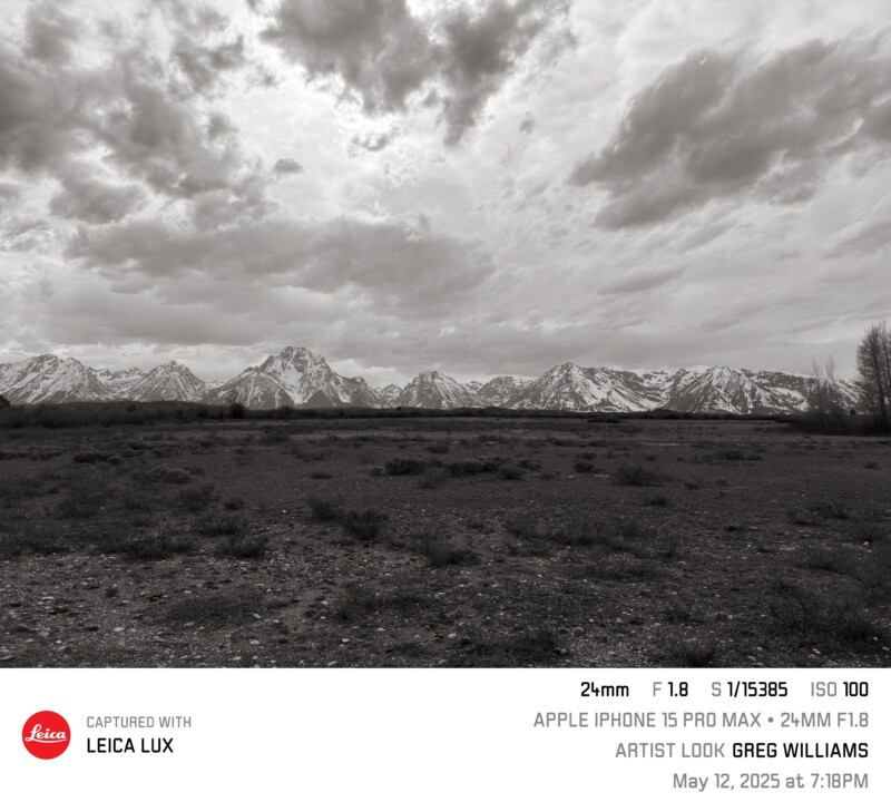 A black-and-white landscape photo shows dramatic clouds over snow-capped mountains and a dark, empty plain. Technical camera details are overlaid at the bottom, with text crediting Leica Lux and artist Greg Williams.