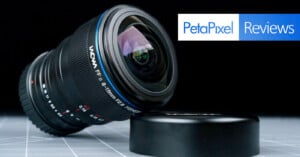 A Laowa 8-15mm f/2.8 fisheye camera lens lies on its side next to its lens cap on a grid-patterned surface, with the PetaPixel Reviews logo in the background.