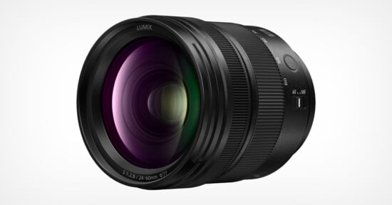 A black Lumix camera lens with purple and green reflections on the glass, shown against a plain white background. The lens has textured focus and zoom rings and labeled focal length markings.