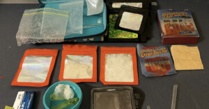 A variety of plastic bags and pouches containing white powders, a digital scale, measuring spoons, and packaging materials arranged on a table.
