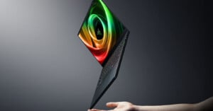A thin, open laptop with a colorful spiral display hovers above an outstretched hand against a dark, gradient background.