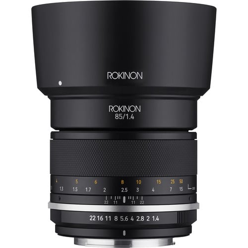 A black Rokinon 85mm f/1.4 camera lens with a focus ring, aperture markings, and a lens hood attached, viewed from the front against a white background.