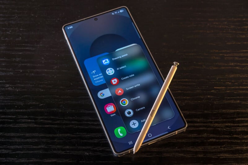 A smartphone with a stylus rests on a dark wooden surface. The phone screen displays a pop-up menu with app shortcuts and settings.