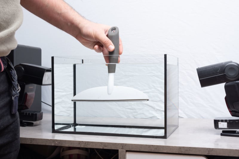 Fish tank filled with water and person removing bubbles from sides