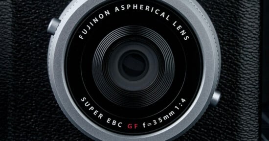 Close-up of a Fujinon Aspherical Lens. The text on the lens reads "FUJINON ASPHERICAL LENS, SUPER EBC GF f=35mm 1:4." The lens is surrounded by a textured black surface.