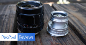 Two camera lenses sit on a wooden surface under natural light. The left lens is black with a red marking, and the right lens is silver. The image features a "PetaPixel Reviews" label in the bottom left corner.