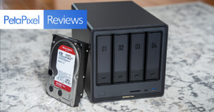 A black four-bay network attached storage device sits on a carpet next to a 4TB hard drive. A “PetaPixel Reviews” banner appears in the upper left corner of the image.