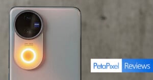 Close-up of a smartphone's rear camera with a prominent circular camera unit featuring a Zeiss lens. A ring light around the camera glows orange. The text "PetaPixel Reviews" is displayed in the bottom right corner on a gray background.