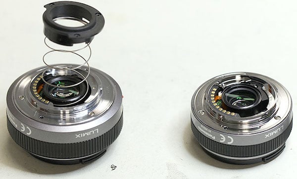 Two Lumix camera lenses are shown. One lens is intact, while the other has its rear mount, spring, and electronic contacts detached and placed above it, revealing its internal components.